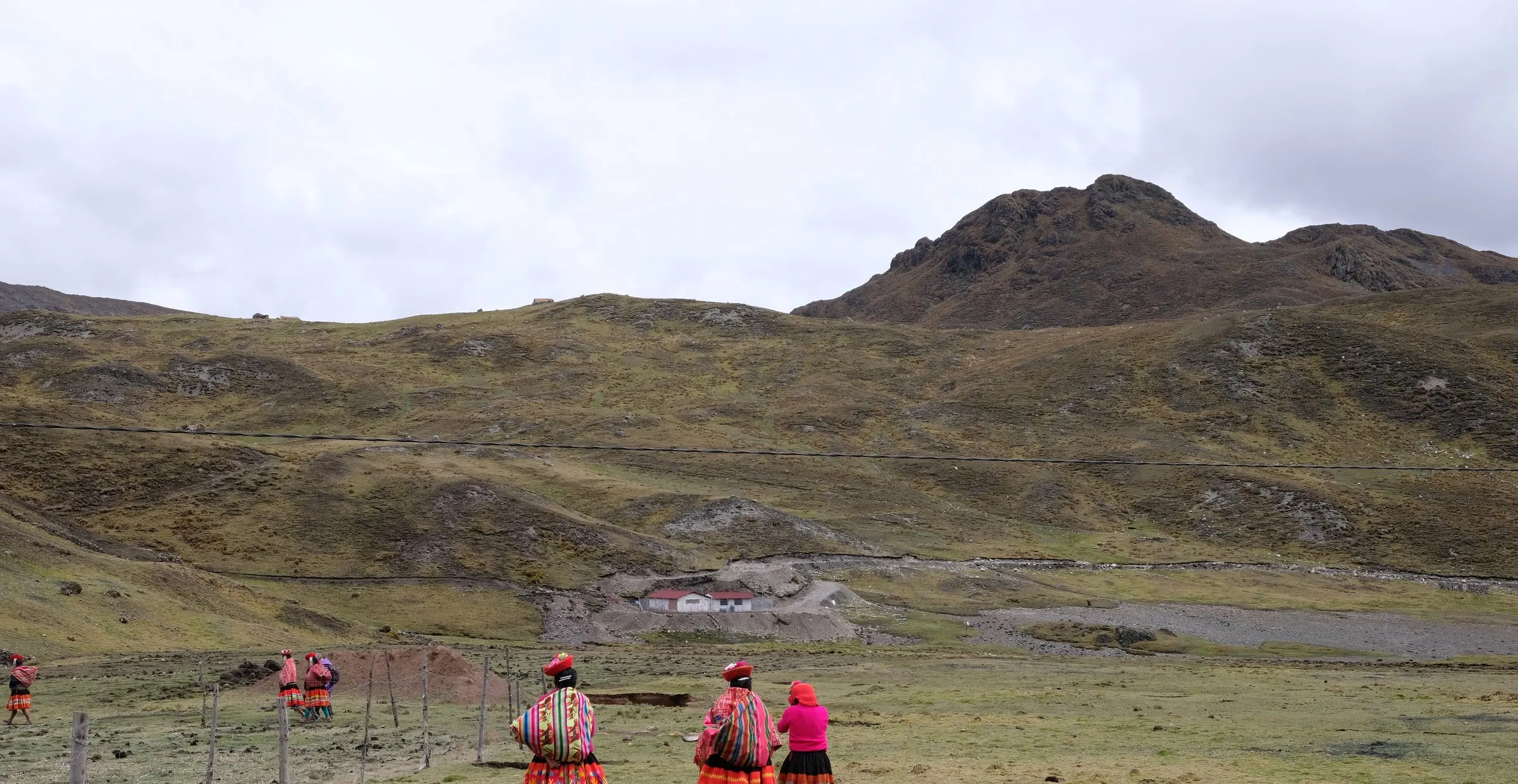 Gruppe in traditioneller Andenkleidung unterwegs auf einer Hochebene, dahinter ein Bergzug